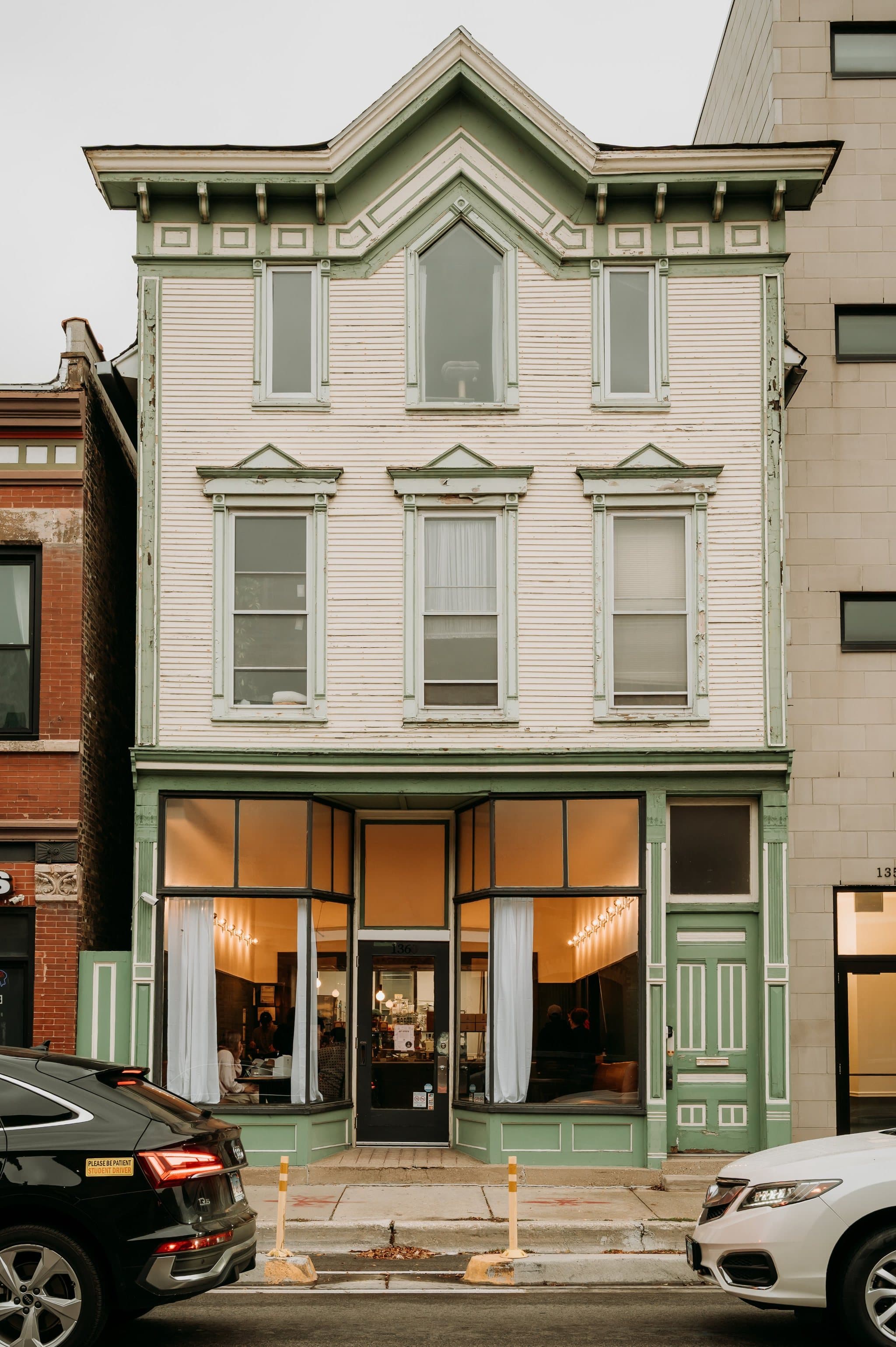 A weathered wood-frame storefront with green trim and lit windows