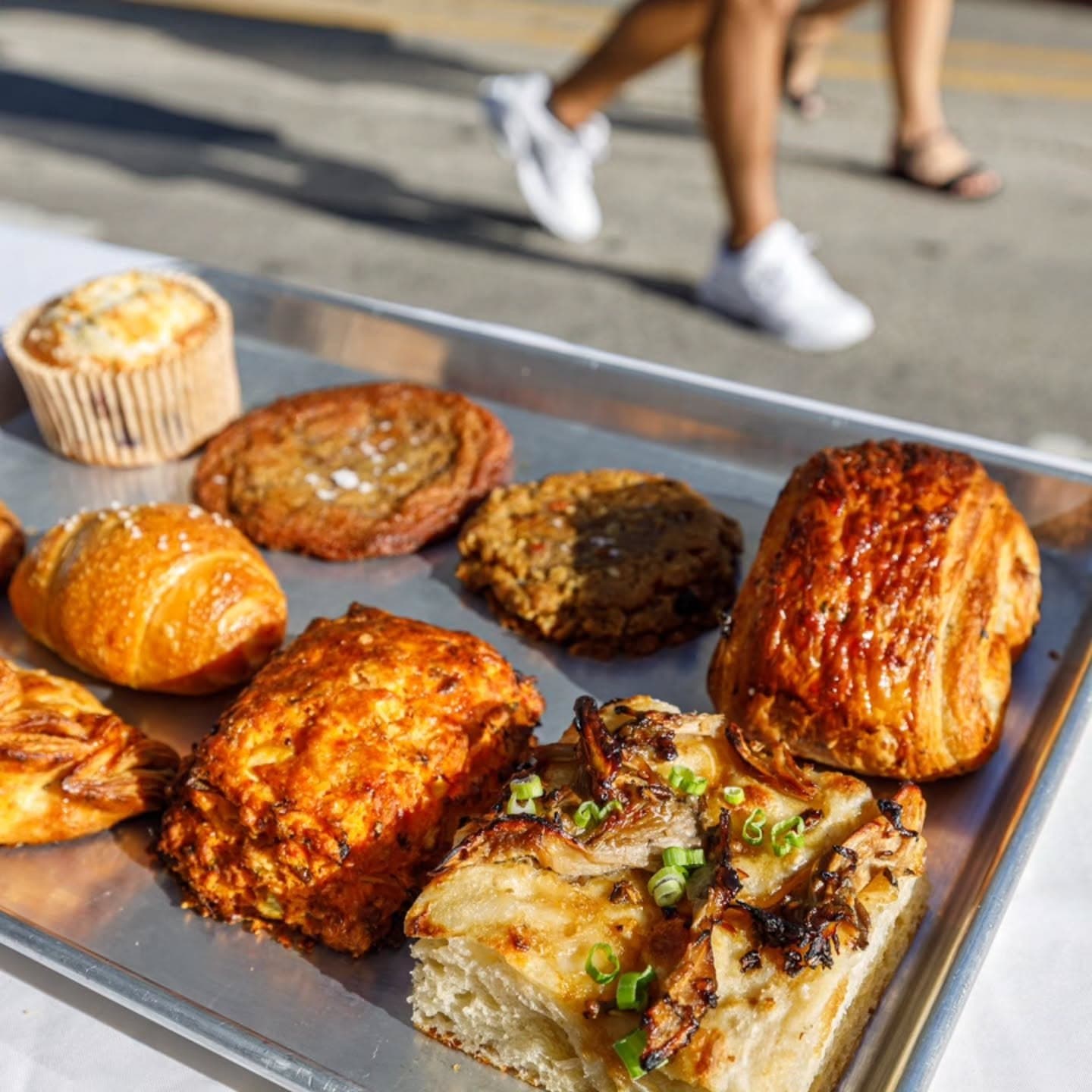 A tray of pastries on the counter as customers pass the window